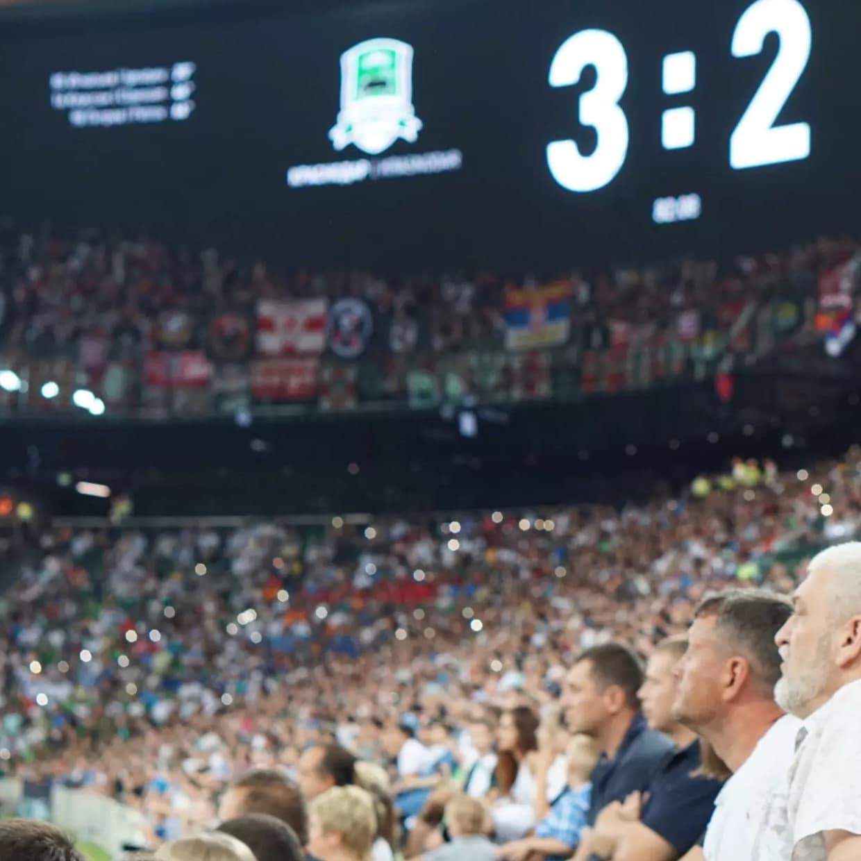 Fans in a stadium under a scoreboard